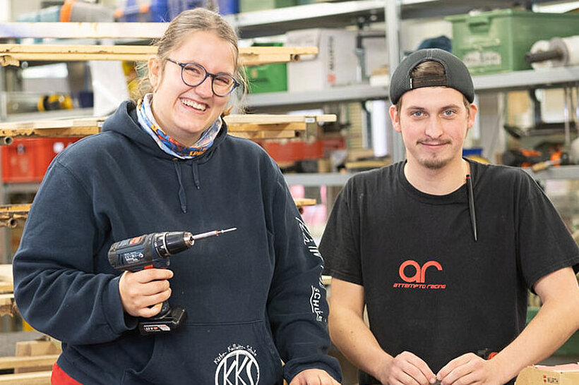 Eine Werkstattmitarbeiterin und ein Werkstattmitarbeiter der Tischlerei stehen nebeneinander und blicken in die Kamera.